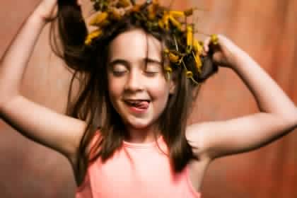 little girl sticking out her tounge wearing a flower crown grinning with her eyes closed holding her hair
