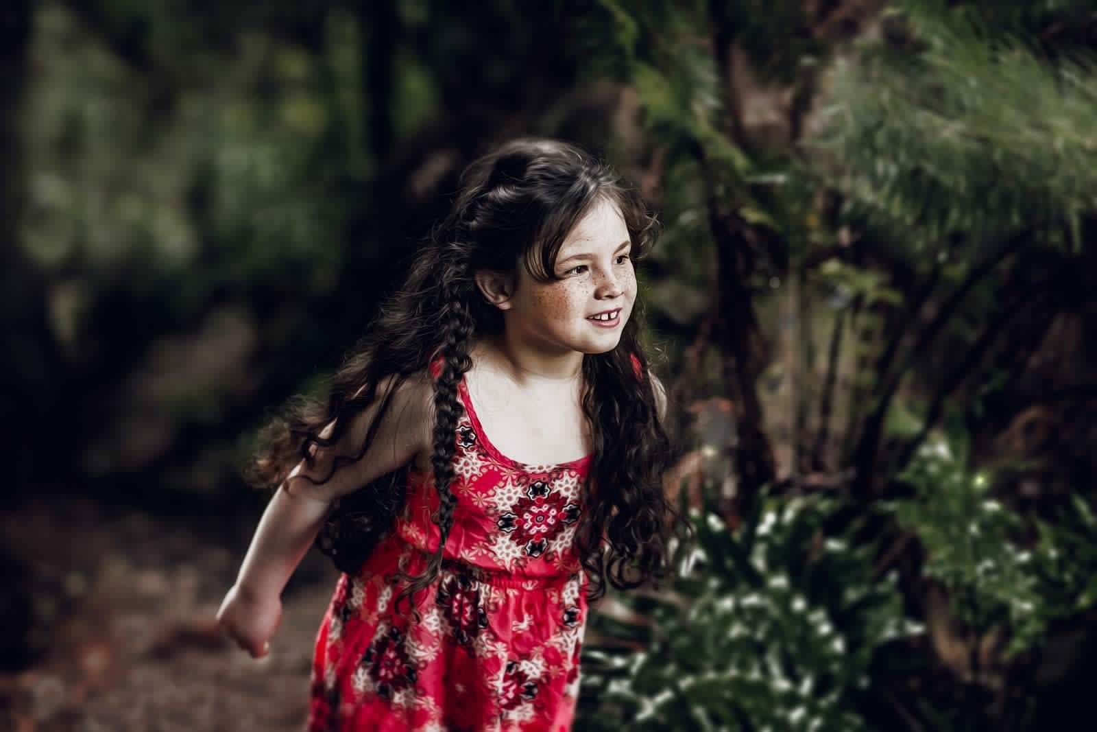tween girl, long dark hair braided, red dress, in a forest looking curious